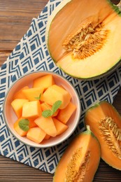 Photo of Pieces of Cantaloupe melon and mint in bowl on wooden table, flat lay