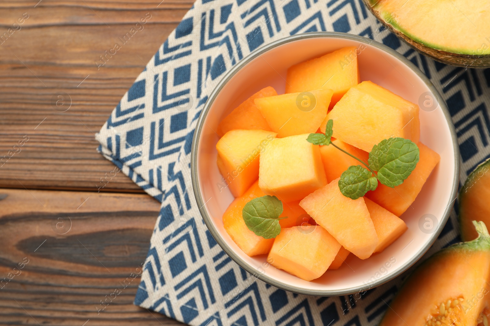 Photo of Pieces of Cantaloupe melon and mint in bowl on wooden table, flat lay. Space for text