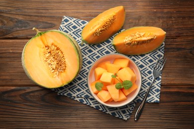 Photo of Tasty ripe Cantaloupe melons and fork on wooden table, flat lay