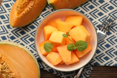 Pieces of ripe Cantaloupe melon in bowl and fork on table, flat lay