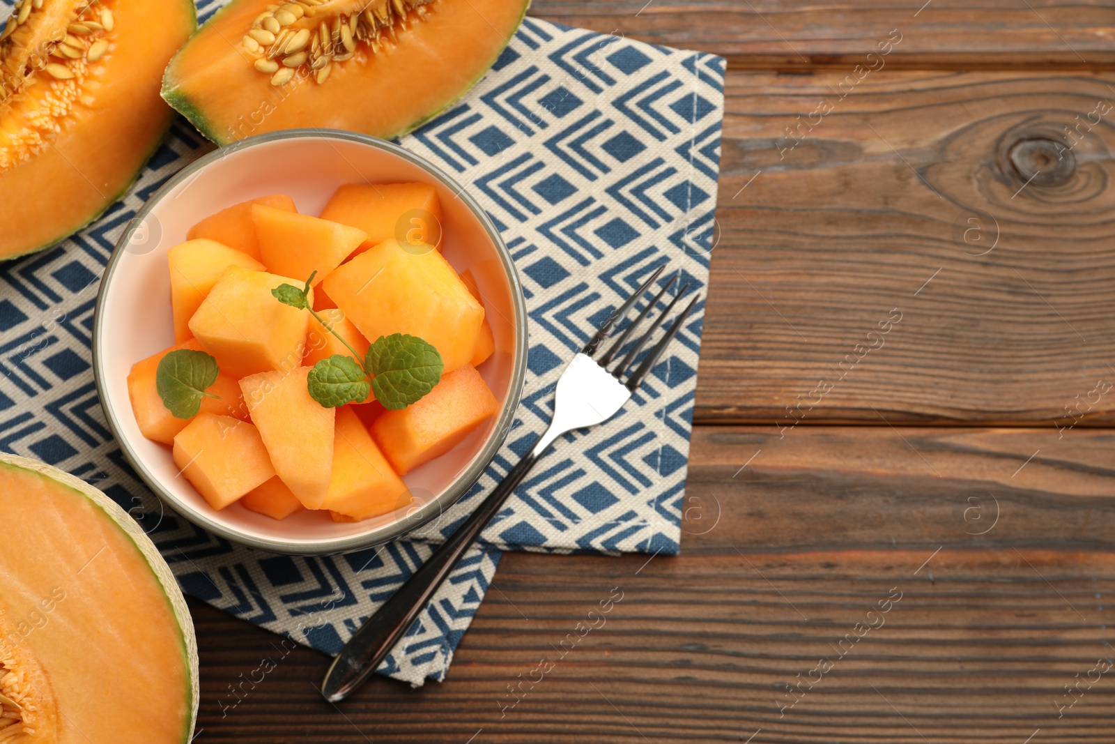 Photo of Pieces of ripe Cantaloupe melon in bowl and fork on wooden table, flat lay. Space for text