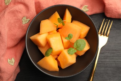 Pieces of ripe Cantaloupe melon in bowl and fork on dark wooden table, flat lay