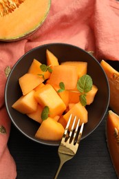 Photo of Pieces of ripe Cantaloupe melon in bowl and fork on dark wooden table, flat lay