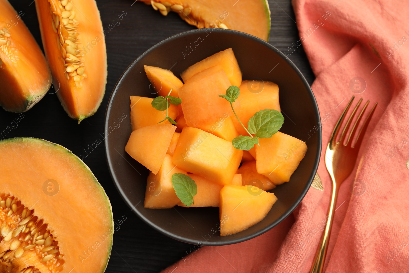 Photo of Pieces of ripe Cantaloupe melon in bowl and fork on dark wooden table, flat lay