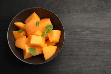 Pieces of ripe Cantaloupe melon and mint in bowl on dark wooden table, top view. Space for text