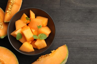 Photo of Pieces of ripe Cantaloupe melon and mint in bowl on dark wooden table, flat lay. Space for text