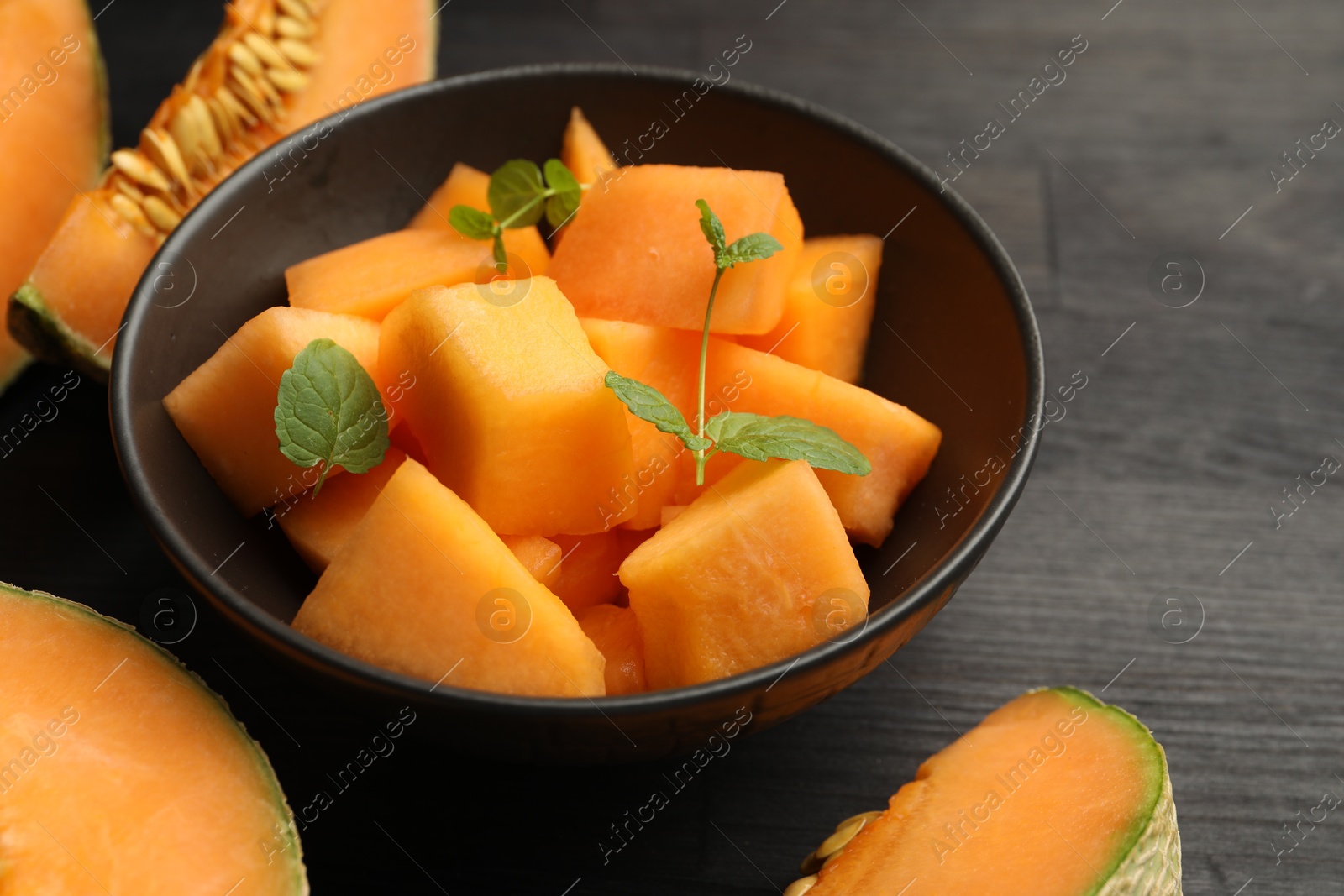 Photo of Pieces of ripe Cantaloupe melon in bowl on dark wooden table, closeup