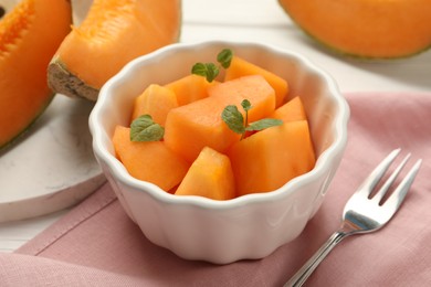 Pieces of ripe Cantaloupe melon in bowl and fork on table, closeup