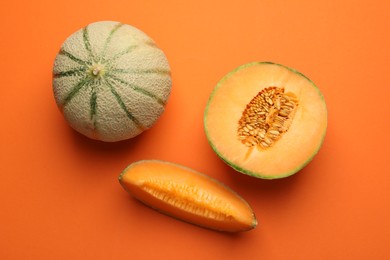 Cut and whole Cantaloupe melons on orange table, flat lay