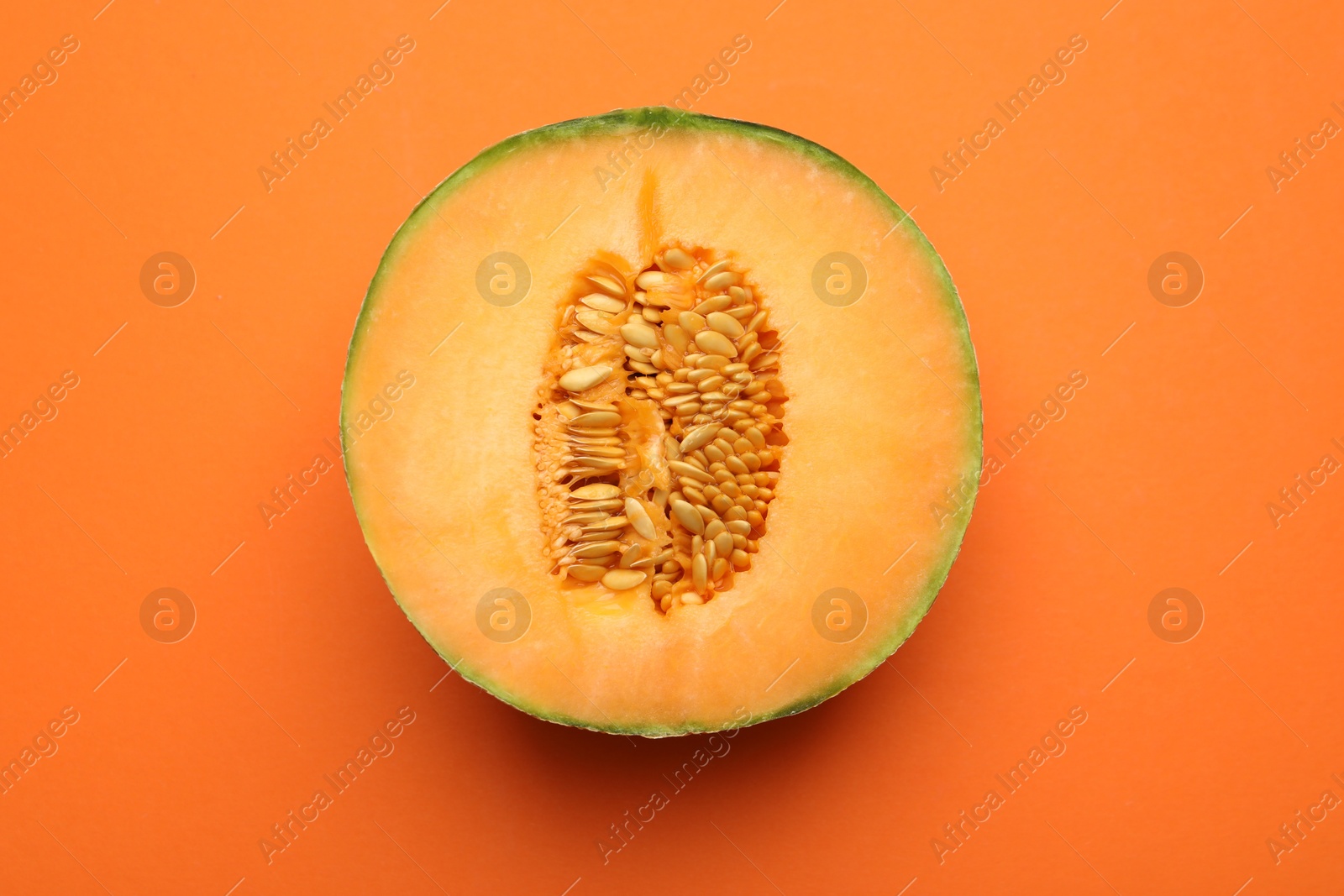 Photo of Half of fresh Cantaloupe melon on orange table, top view