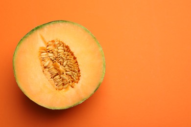 Photo of Half of fresh Cantaloupe melon on orange table, top view. Space for text