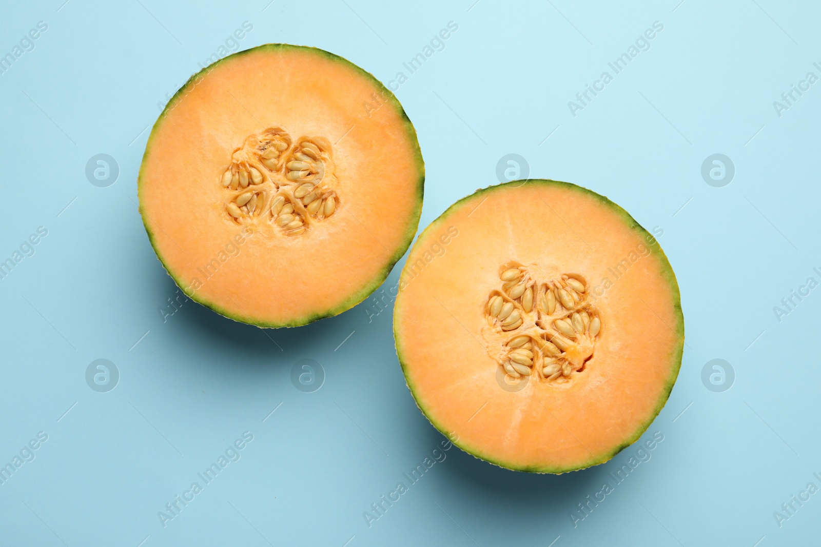 Photo of Halves of fresh Cantaloupe melon on light blue table, flat lay