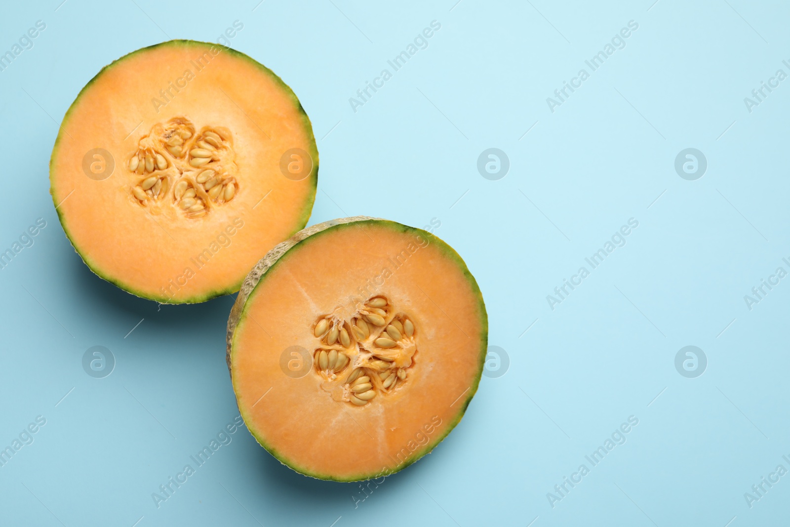 Photo of Halves of fresh Cantaloupe melon on light blue table, flat lay. Space for text