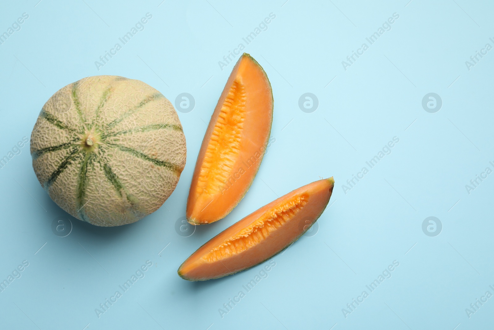 Photo of Cut and whole Cantaloupe melons on light blue table, flat lay. Space for text