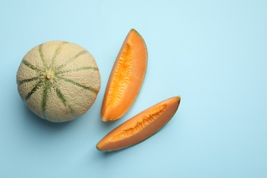 Cut and whole Cantaloupe melons on light blue table, flat lay. Space for text