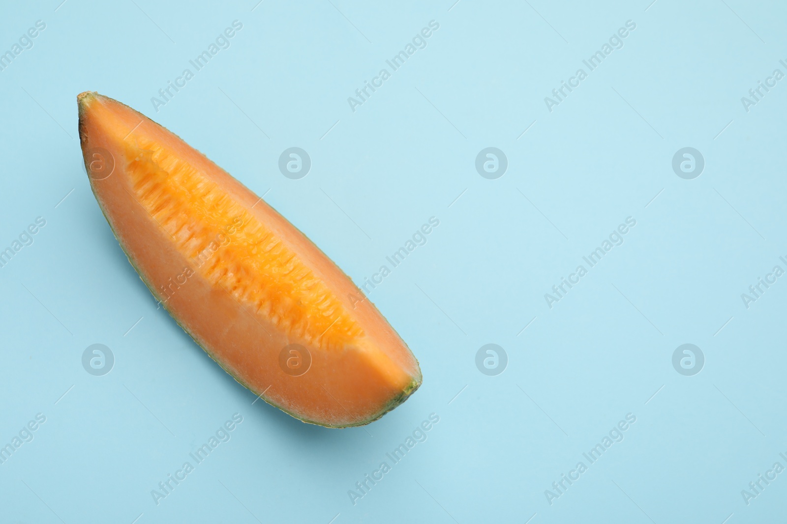 Photo of Piece of fresh Cantaloupe melon on light blue table, top view. Space for text