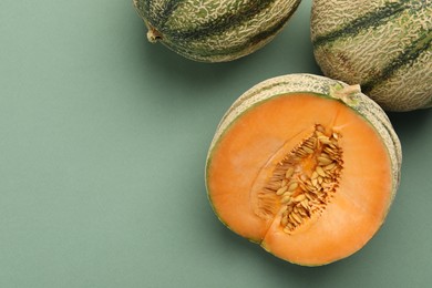 Photo of Cut and whole Cantaloupe melons on green table, flat lay. Space for text