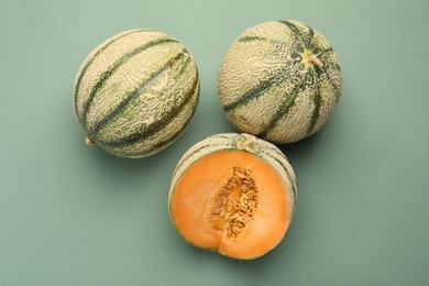 Cut and whole Cantaloupe melons on green table, flat lay