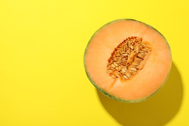 Photo of Half of fresh Cantaloupe melon on yellow table, top view. Space for text