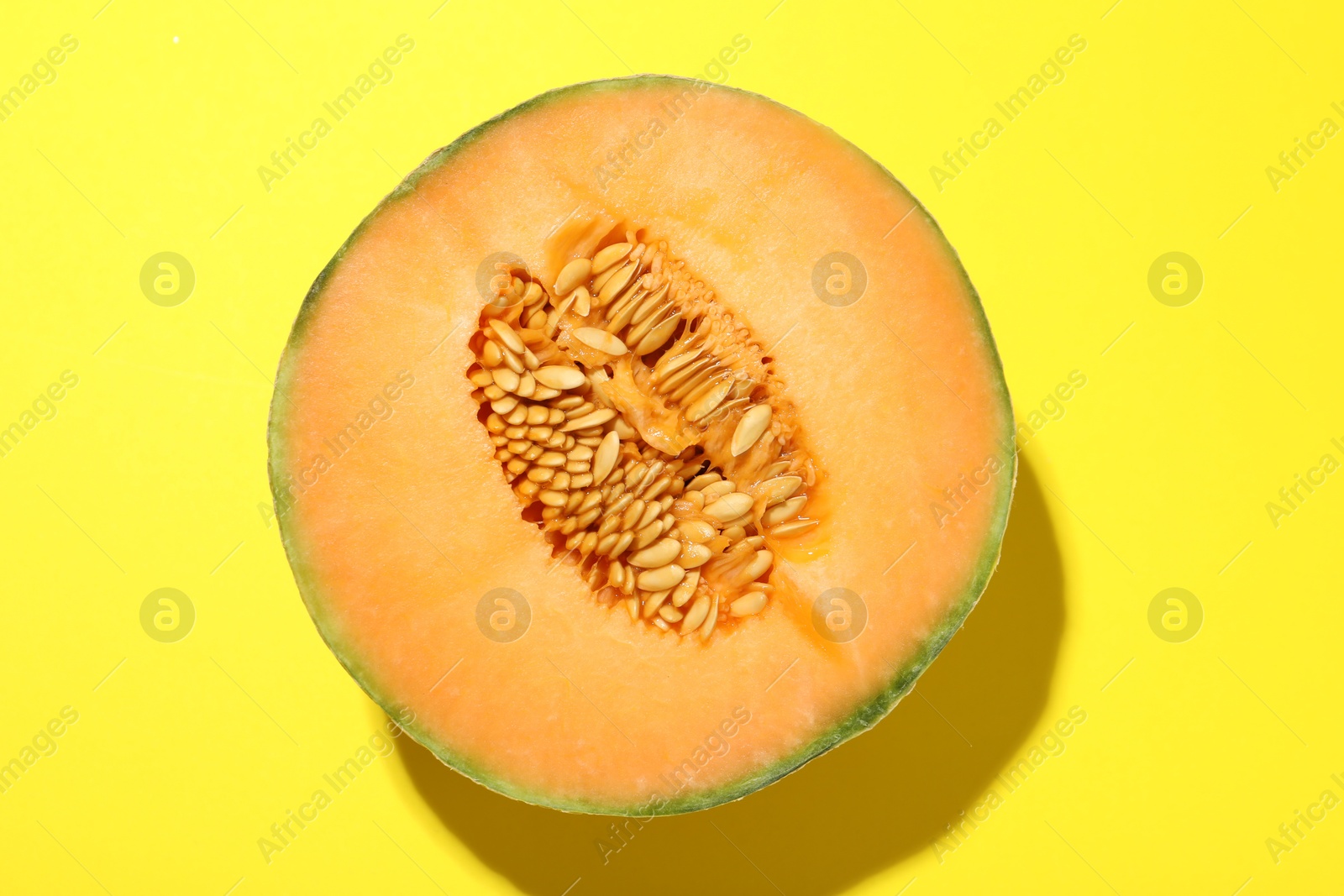 Photo of Half of fresh Cantaloupe melon on yellow table, top view