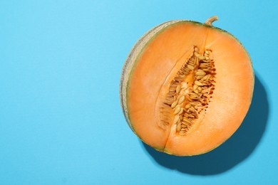 Photo of Half of fresh Cantaloupe melon on light blue table, top view. Space for text