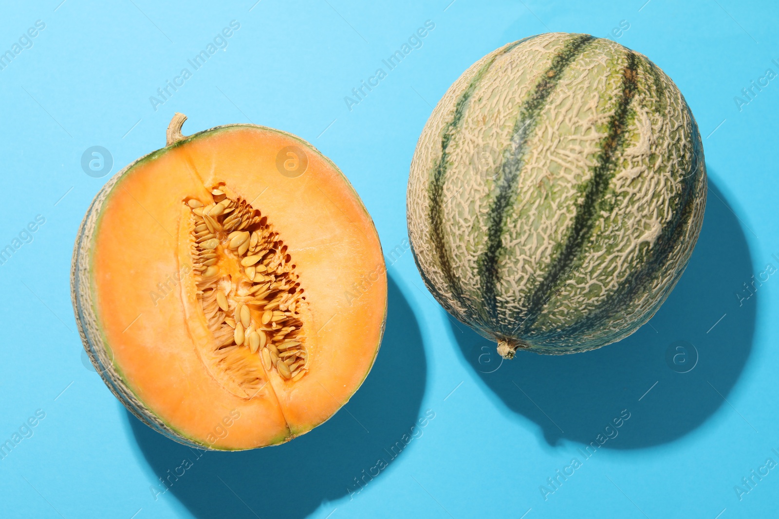 Photo of Cut and whole Cantaloupe melons on light blue table, flat lay