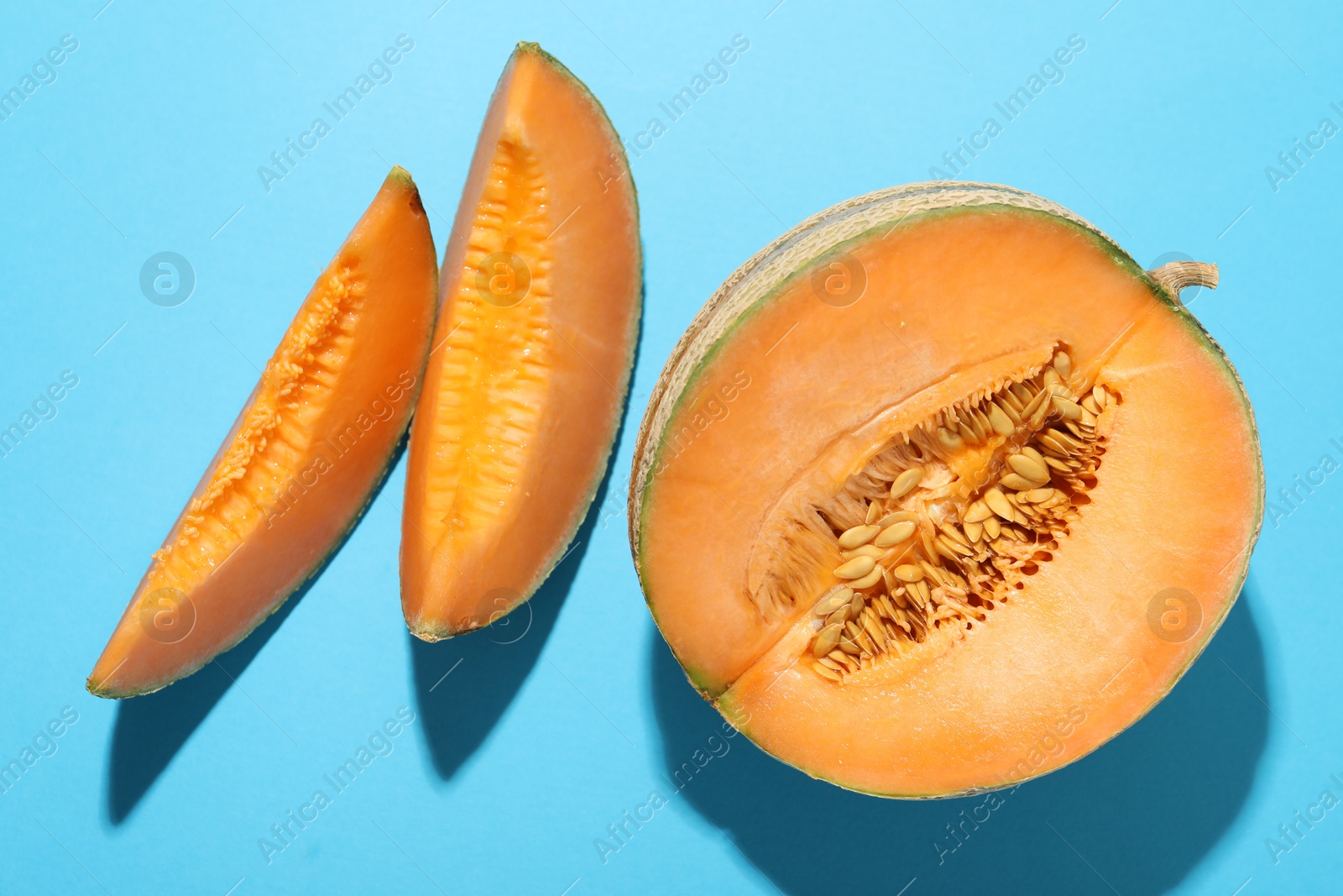 Photo of Pieces of fresh Cantaloupe melon on light blue table, flat lay