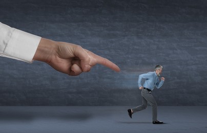 Image of Big hand pointing at running away small businessman on grey background. Authority, abuse concepts