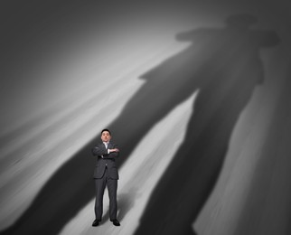 Businessman standing in his own huge shadow on grey background. Ego, inner power concepts