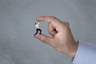 Big hand holding small businessman on grey background. Authority, abuse, conflict concepts