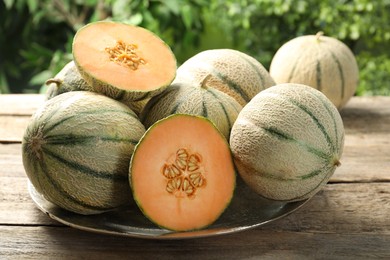 Whole and cut ripe Cantaloupe melons on wooden table outdoors, closeup