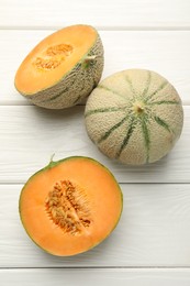 Photo of Whole and cut ripe Cantaloupe melons on white wooden table, flat lay