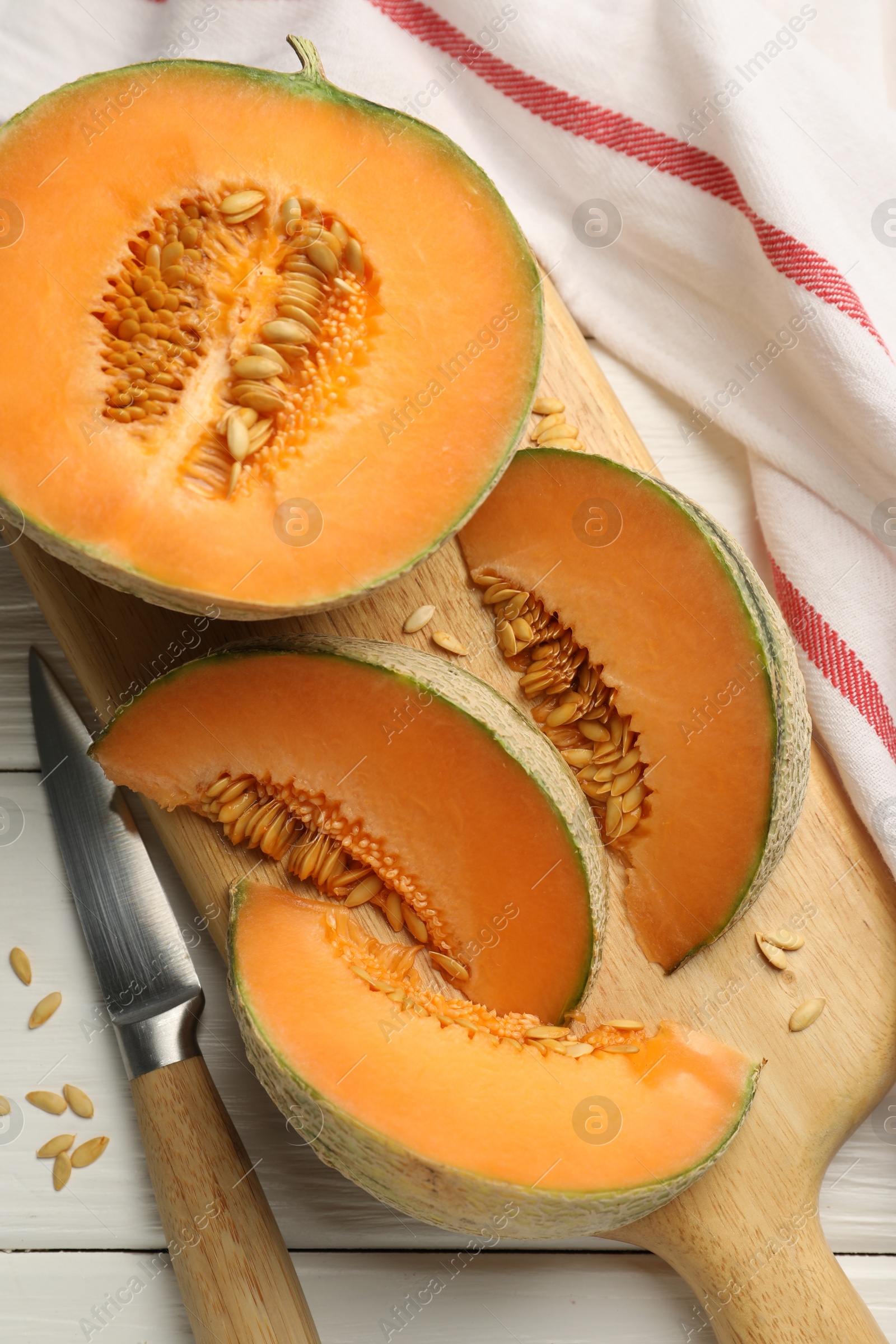 Photo of Cut ripe Cantaloupe melon and knife on white wooden table, flat lay