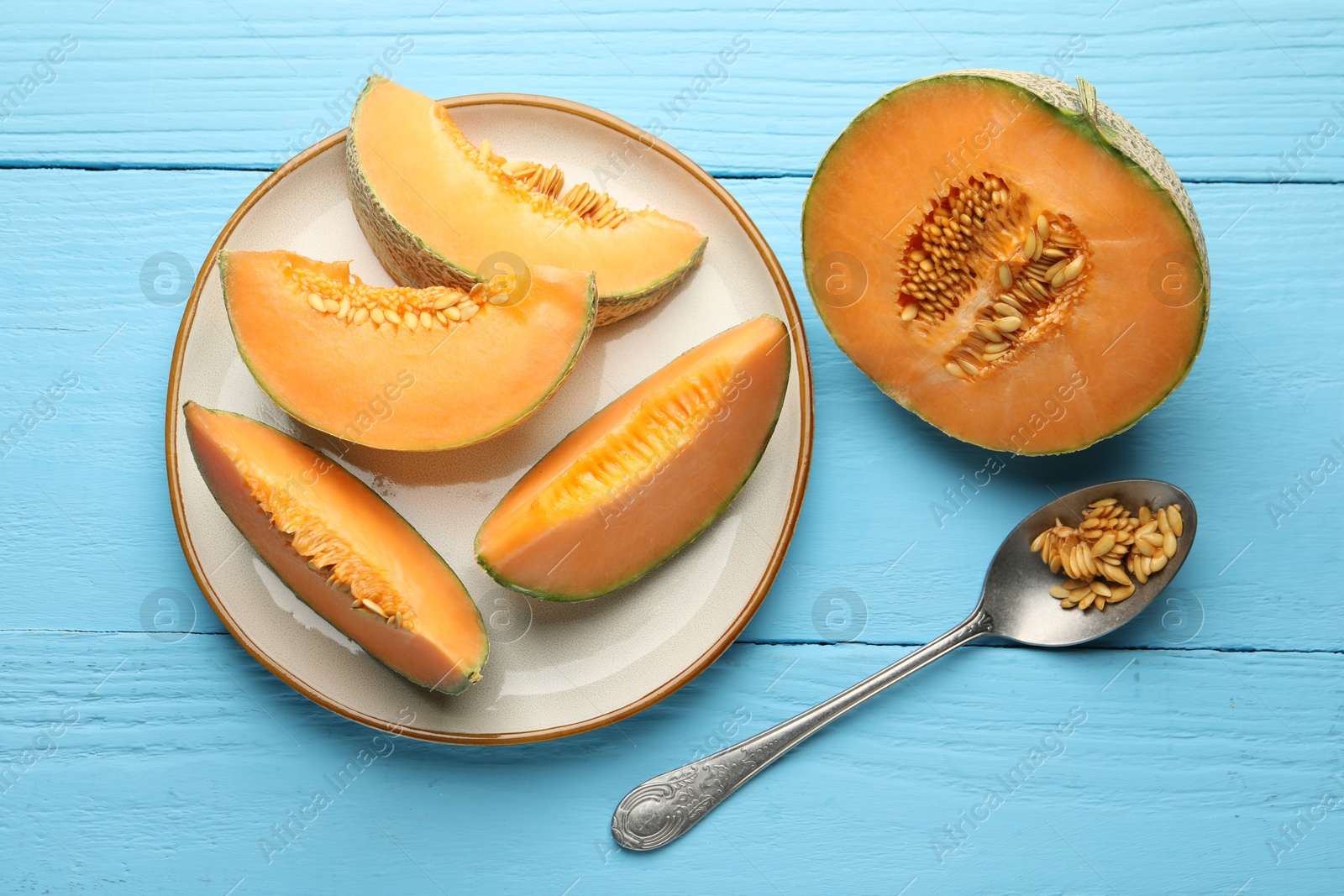 Photo of Cut ripe Cantaloupe melon and spoon with seeds on light blue wooden table, flat lay