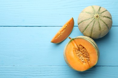 Cut and whole ripe Cantaloupe melons on light blue wooden table, flat lay. Space for text