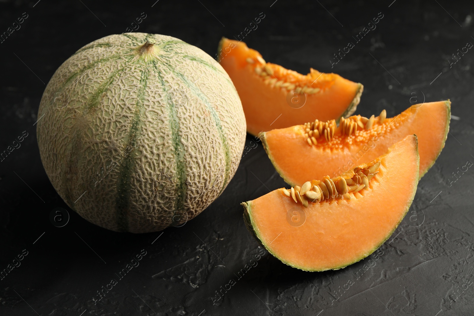 Photo of Cut and whole ripe Cantaloupe melons on dark textured table