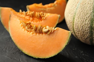 Photo of Cut and whole ripe Cantaloupe melons on dark textured table, closeup