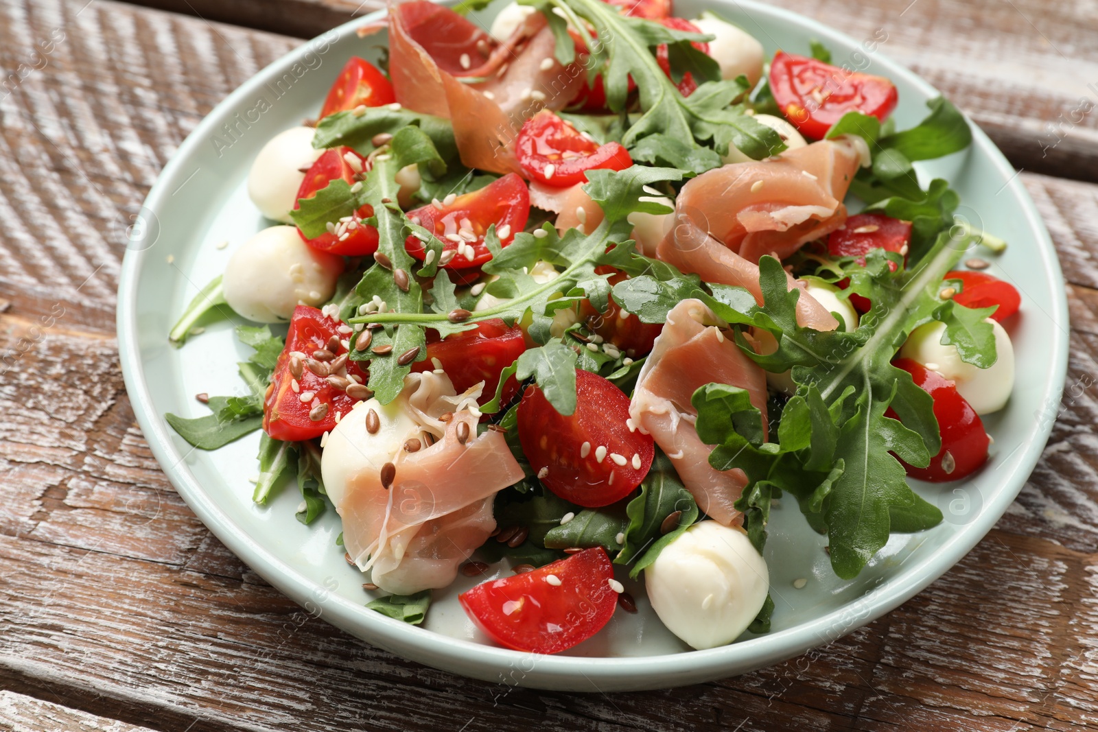 Photo of Tasty salad with arugula, mozzarella cheese, tomatoes and jamon on wooden table, closeup