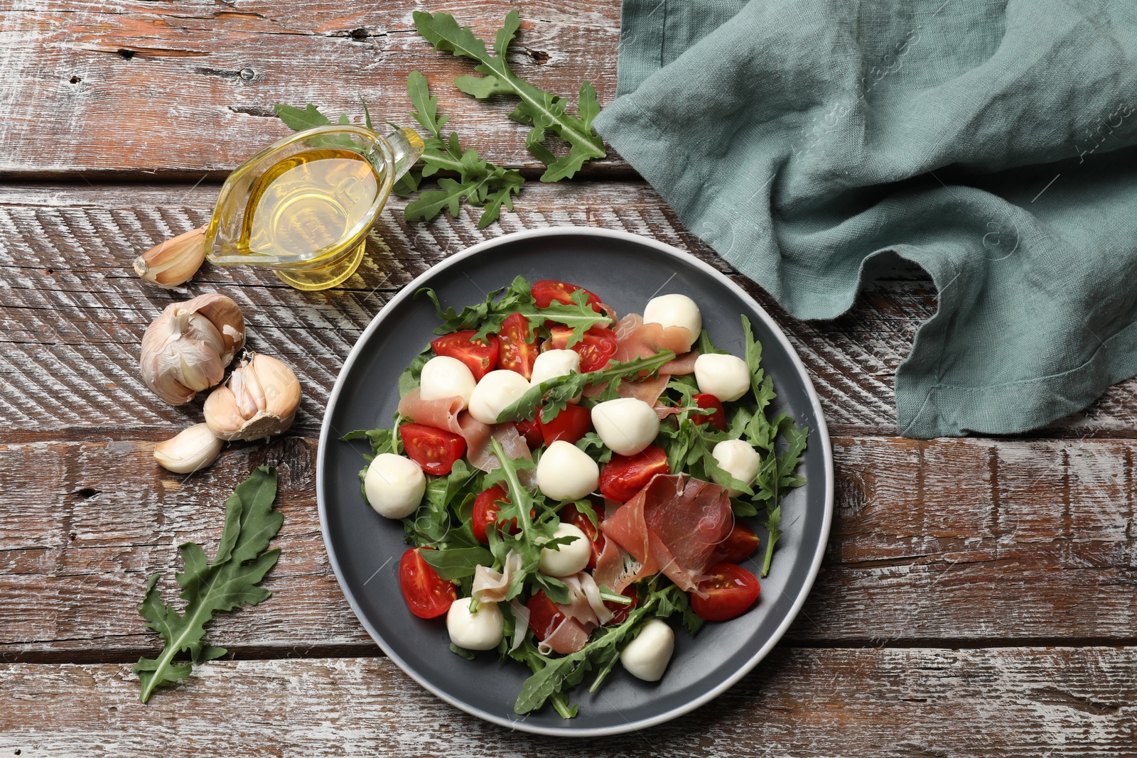 Photo of Tasty salad with arugula, mozzarella cheese, tomatoes and jamon on wooden table, flat lay