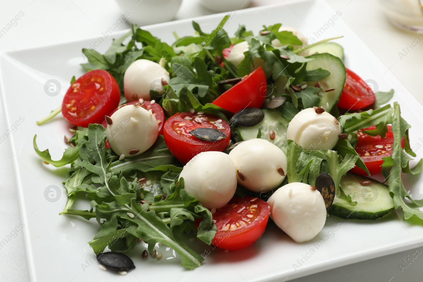 Photo of Tasty salad with arugula, mozzarella cheese and vegetables on white table, closeup