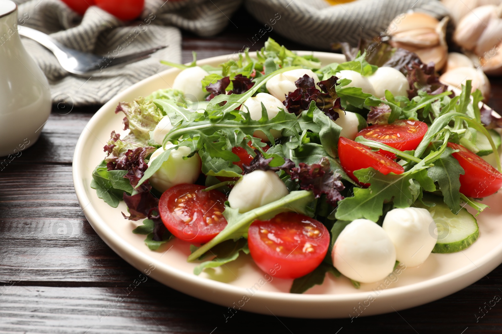 Photo of Tasty salad with arugula, lettuce, mozzarella cheese and vegetables on wooden table, closeup