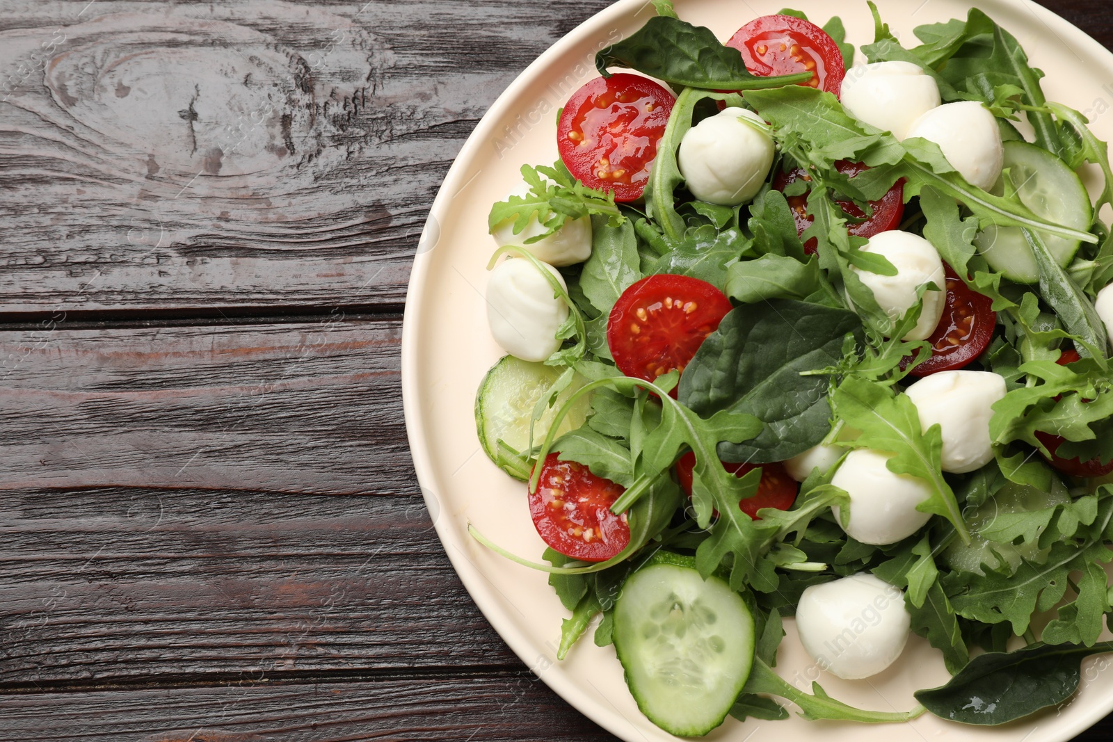 Photo of Tasty salad with arugula, spinach, mozzarella cheese and vegetables on wooden table, top view. Space for text