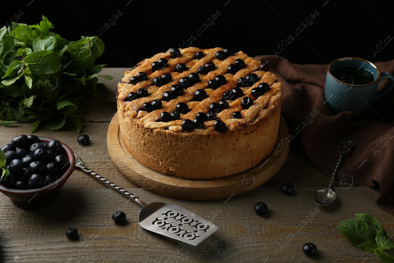 Photo of Homemade blueberry pie, fresh berries, cake server and mint on wooden table