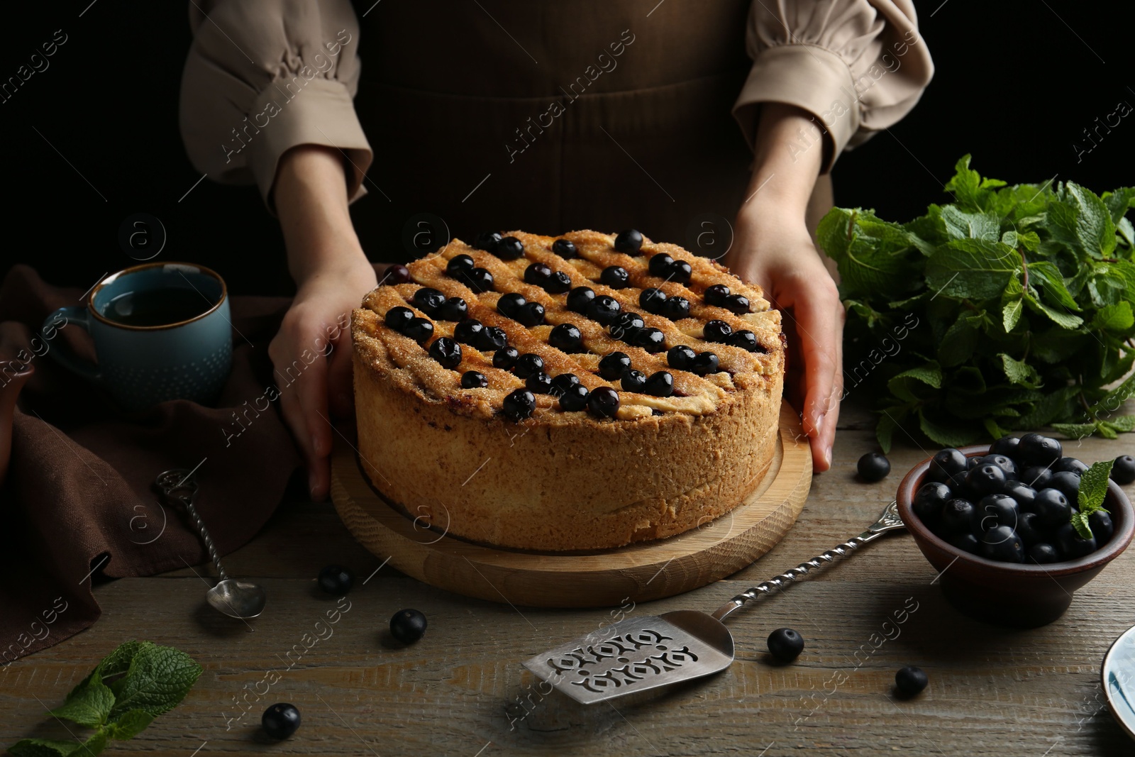 Photo of Woman with homemade blueberry pie at wooden table, closeup