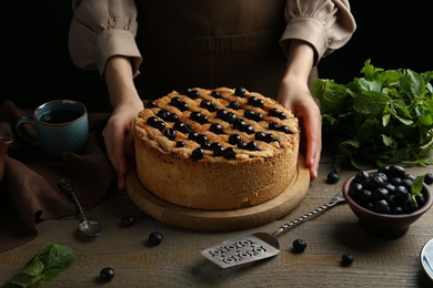 Photo of Woman with homemade blueberry pie at wooden table, closeup