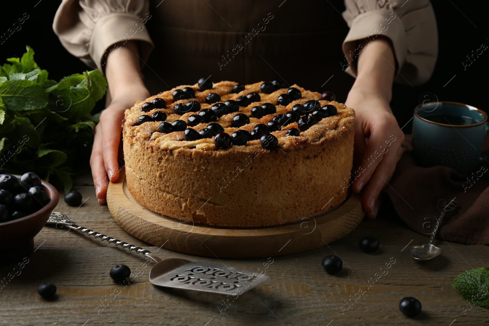 Photo of Woman with homemade blueberry pie at wooden table, closeup