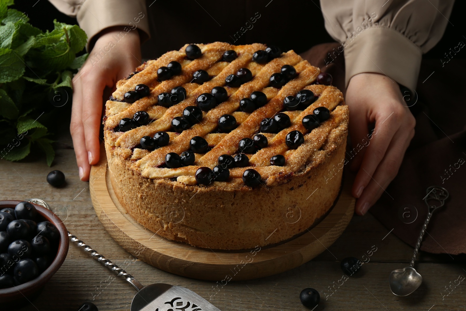 Photo of Woman with homemade blueberry pie at wooden table, closeup