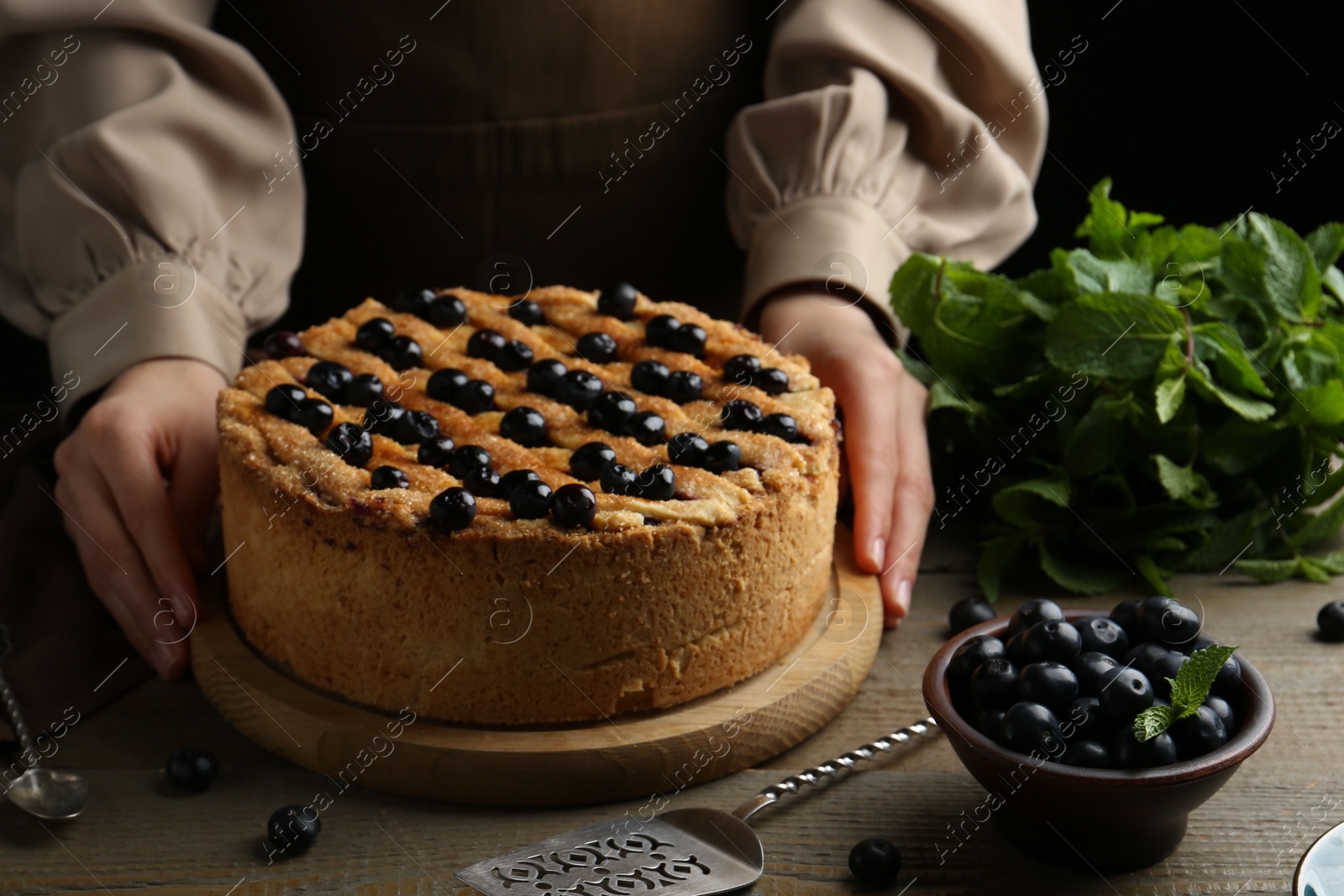 Photo of Woman with homemade blueberry pie at wooden table, closeup