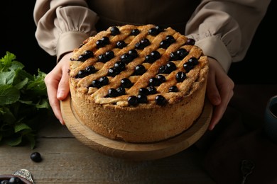 Photo of Woman with homemade blueberry pie at wooden table, closeup