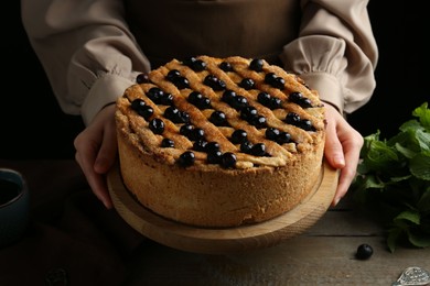 Photo of Woman with homemade blueberry pie at wooden table, closeup